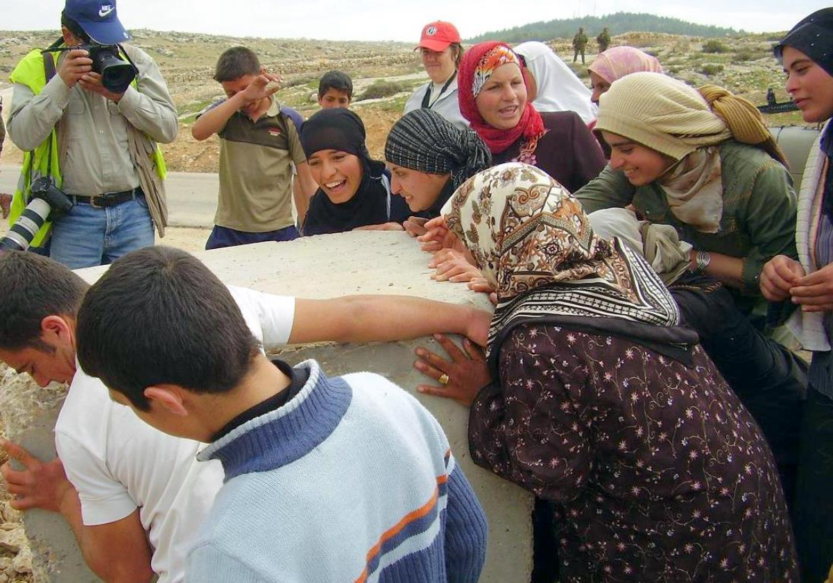 Palestinians remove a roadblock while a member of CPT stands behind them.